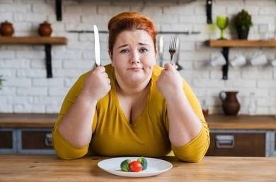 Obesity is complex. Woman sitting in front of a plate with fruit and vegetables.